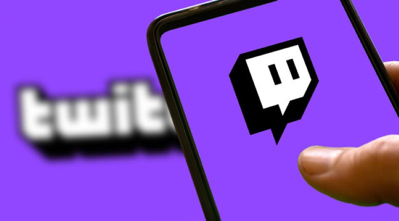 A smartphone held in one hand displaying the Twitch logo on a purple background, symbolizing live streaming content.