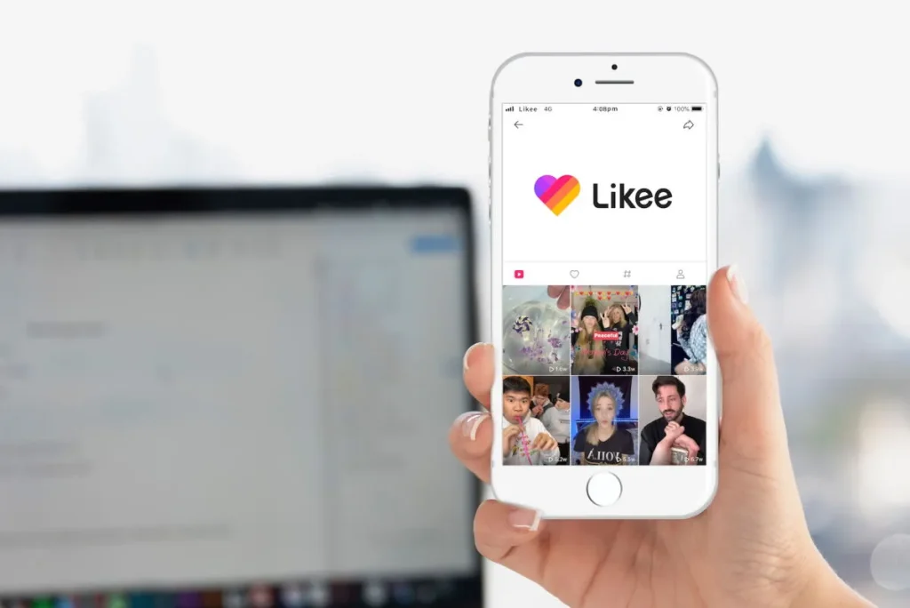 A hand holding a smartphone showing the Likee app home screen with multiple short video thumbnails.