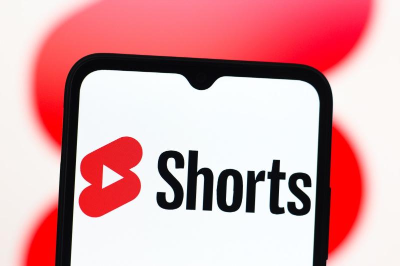 A close-up of a smartphone screen displaying the YouTube Shorts logo on a white background.
