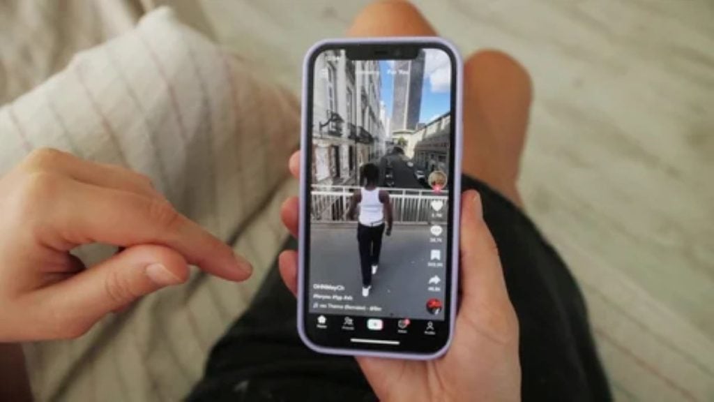 A person holding a smartphone while watching a short-form video in a vertical feed resembling a TikTok-style interface.