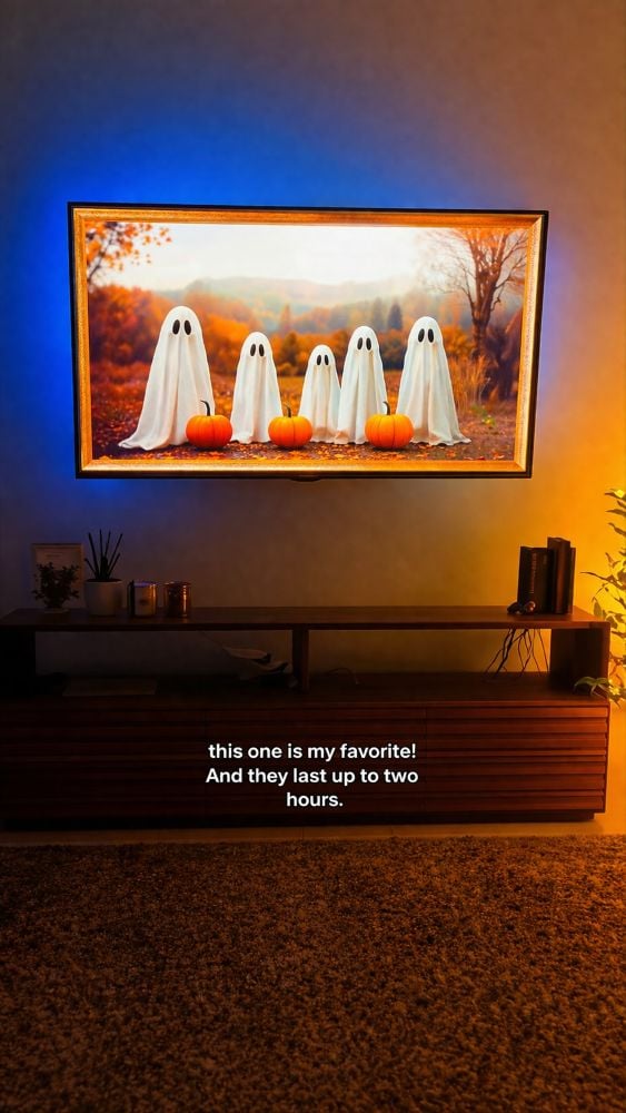 A cozy living room with a wall-mounted TV displaying a vibrant autumn scene of ghost figures and pumpkins, surrounded by warm ambient lighting and modern decor.