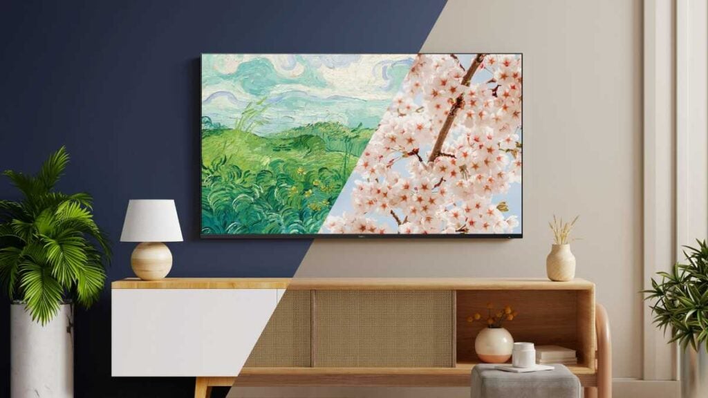 Flat-screen TV mounted on a wall displaying split-screen artwork with a landscape painting and cherry blossoms, styled like a decorative frame TV above a wooden console with plants and home decor.