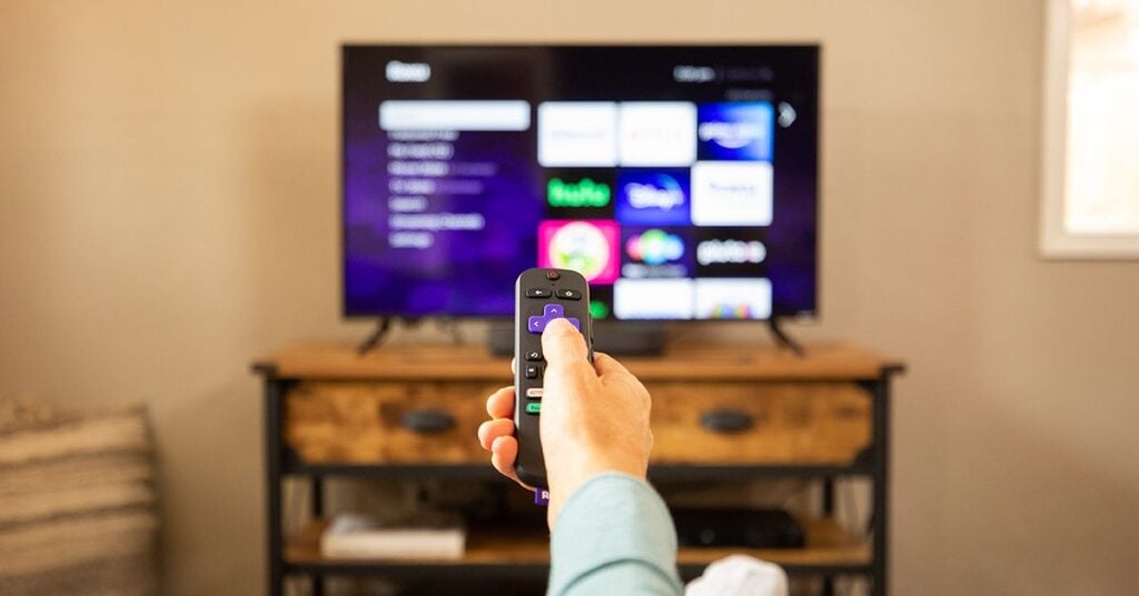 Person holding a remote control while watching a smart TV streaming interface in a cozy living room setting.