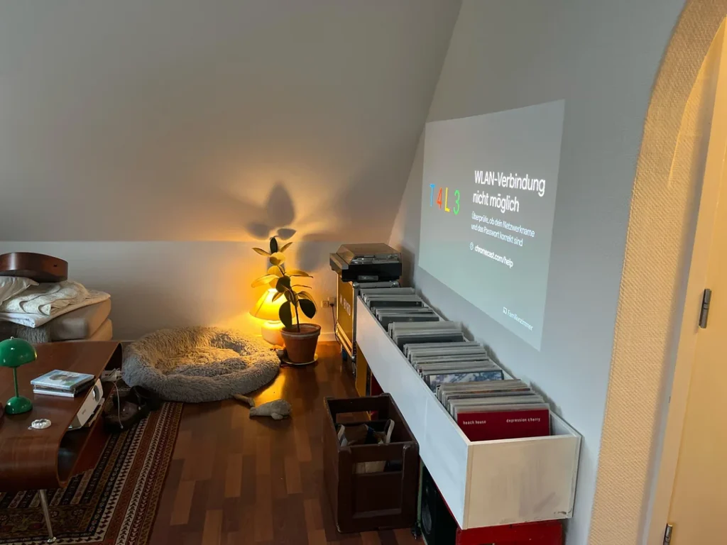 Sloped-ceiling room with a projector casting onto an angled wall above a long vinyl record storage cabinet.