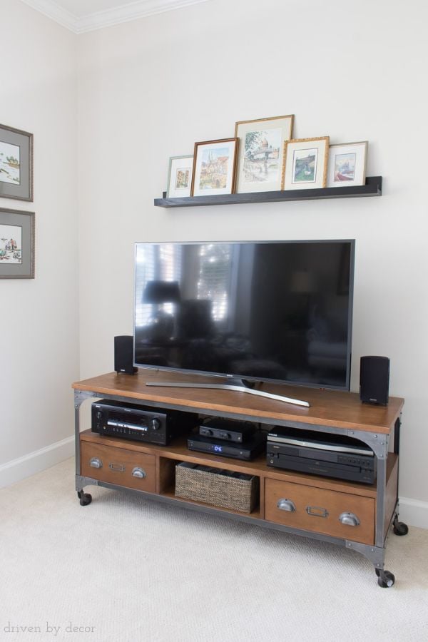 TV console with a slim black picture ledge above the television displaying layered framed art in a simple renter-friendly living room setup.
