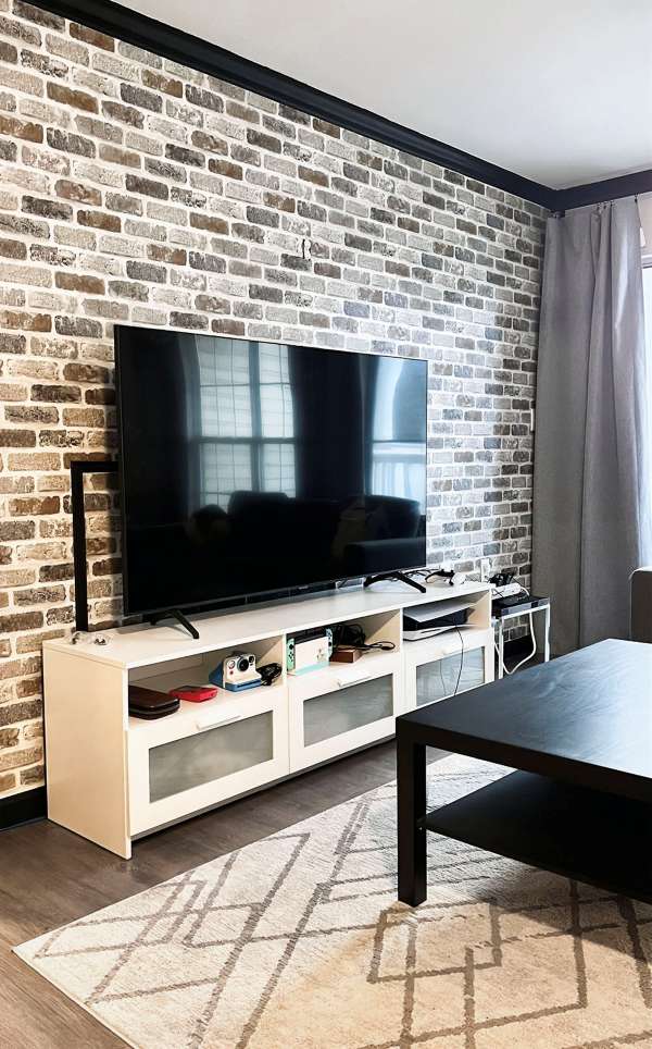 Living room TV wall with peel-and-stick brick wallpaper behind a white media console for a renter-friendly accent wall.