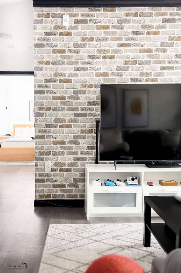 White brick peel-and-stick wallpaper accent wall behind a TV and white media console in a modern living room.