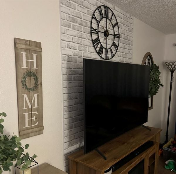 TV console with a white brick wallpaper panel behind the television, styled with a large wall clock and farmhouse wall decor.