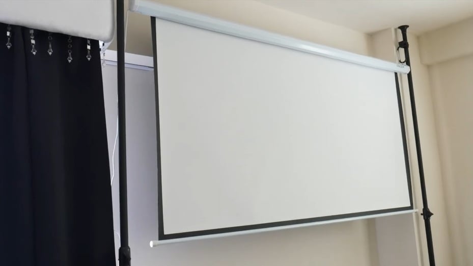 Retractable projector screen mounted on renter-friendly tension rods in front of curtains without drilling into the wall.