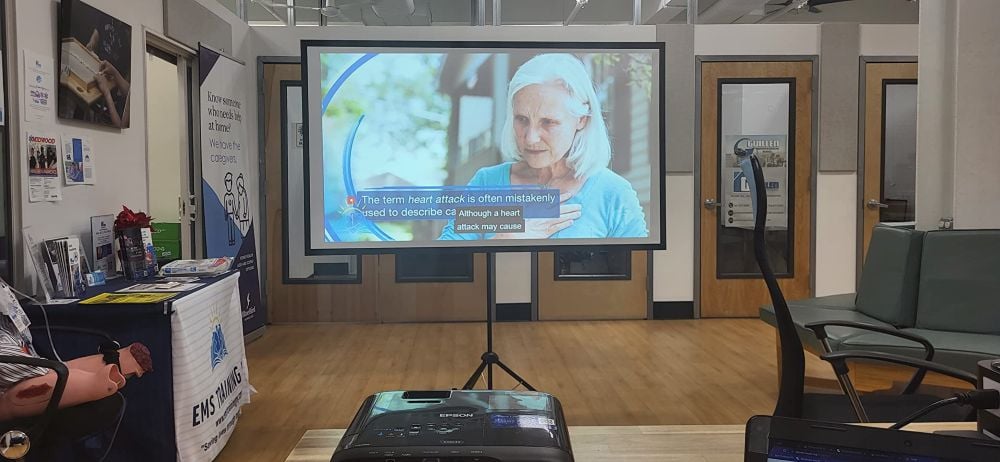 Portable projector screen stand displaying a health presentation in a waiting room or office space with a projector in the foreground.