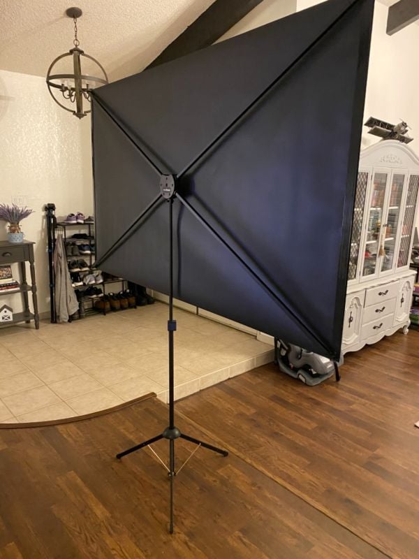 Back view of a portable pull-down projector screen on a tripod stand set up inside a home.