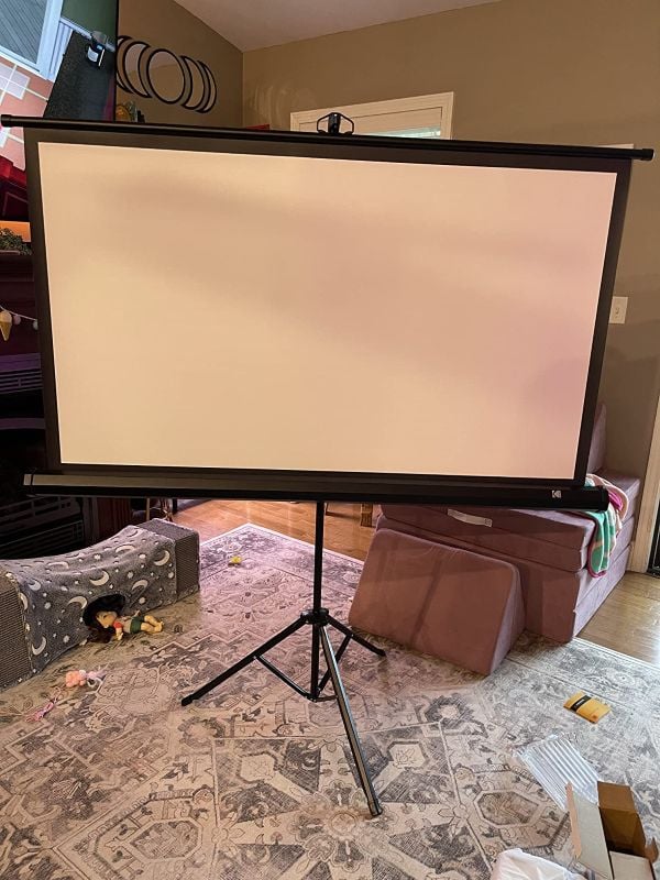 Blank pull-down portable projector screen on a tripod stand set up in a living room play area.