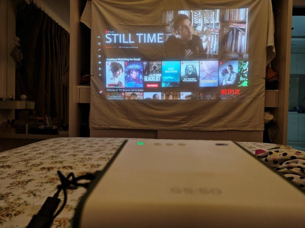 Bedroom projector setup showing Netflix projected onto a white sheet with the projector placed on the bed.