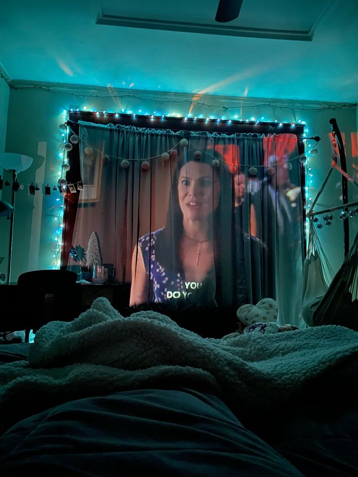 Cozy bedroom projector setup casting a movie onto curtains framed by blue string lights.