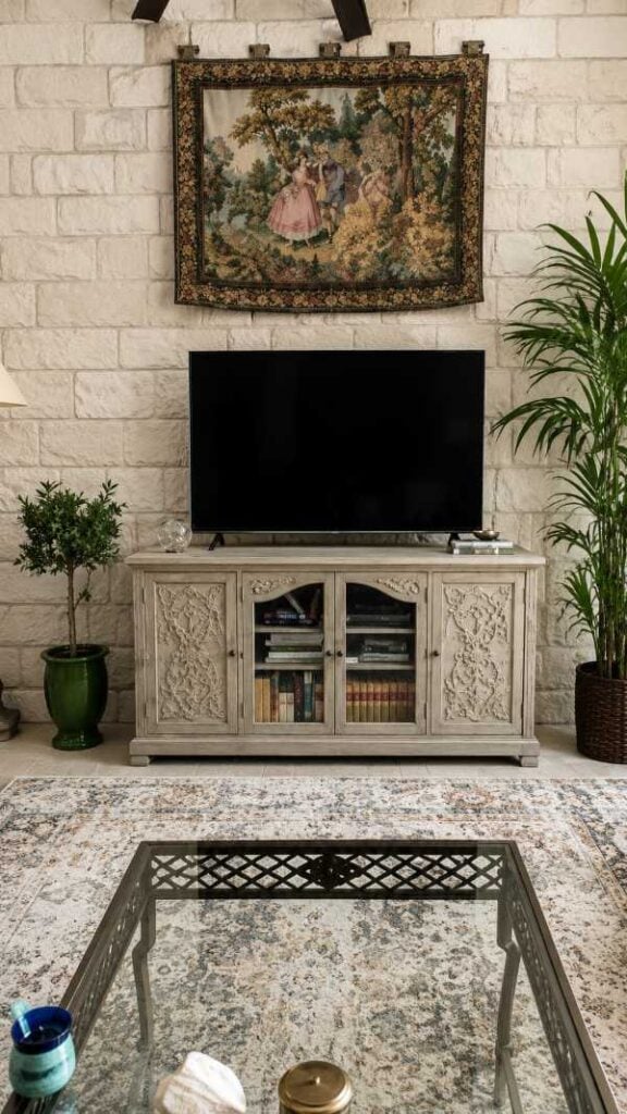 Living room TV setup with a vintage-style fabric wall hanging above the television, framed by a stone accent wall and potted plants.