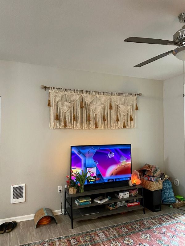 Macrame wall hanging with tassels displayed above a TV and media console in a relaxed boho-style living room.