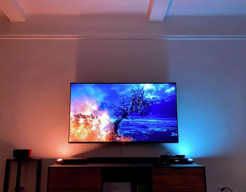 Wall-mounted TV with warm orange and cool blue LED backlighting glowing behind it above a low media console.