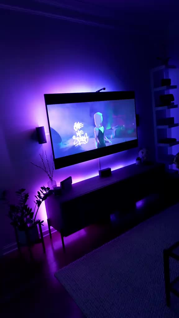 Dark living room with purple LED backlighting around a wall-mounted TV for a moody home theater effect.