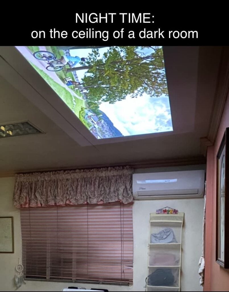 A projector displays a video onto the ceiling of a dark bedroom, with text reading “NIGHT TIME: on the ceiling of a dark room.”