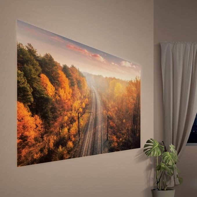 A large peel-and-stick projector screen on a wall displays a scenic autumn railway image in a minimalist room.