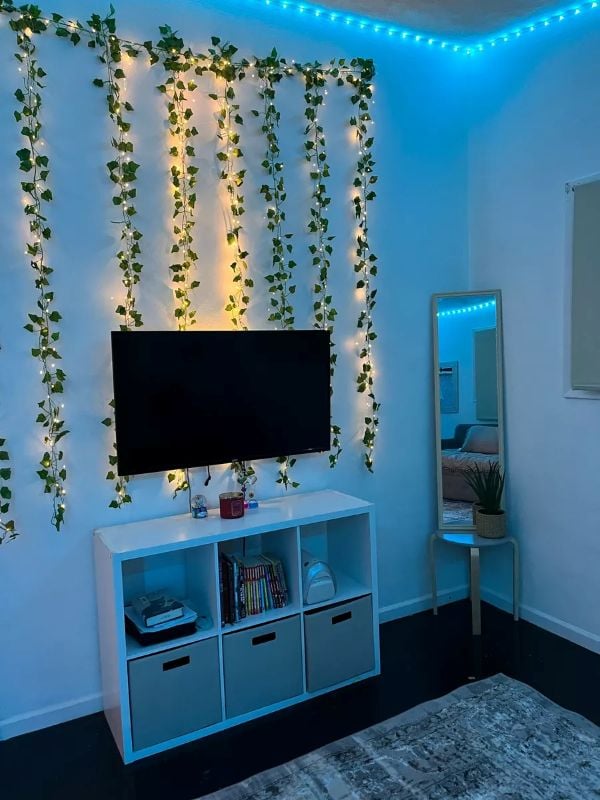 Bedroom TV wall decorated with faux ivy vines, string lights, and blue LED lighting around the ceiling.