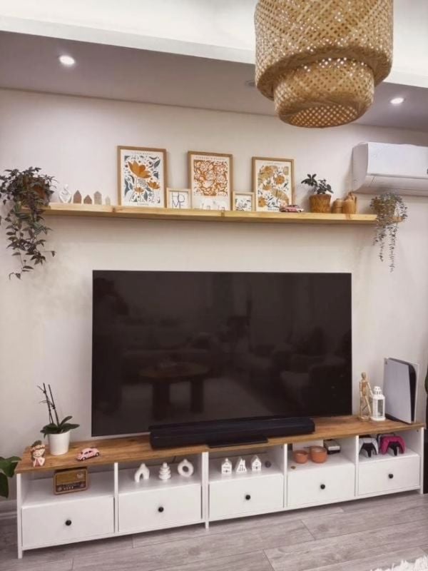 Modern TV wall with a long picture ledge above the television, framed prints, small decor, and potted plants.