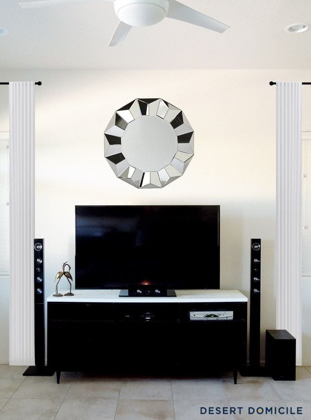 Minimal TV setup with a geometric mirror above the television and black floor speakers on both sides.