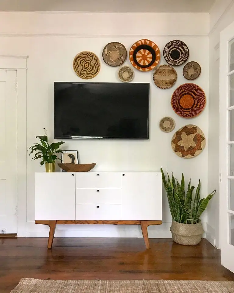 Wall-mounted TV surrounded by woven basket decor above a mid-century white media cabinet with plants nearby.