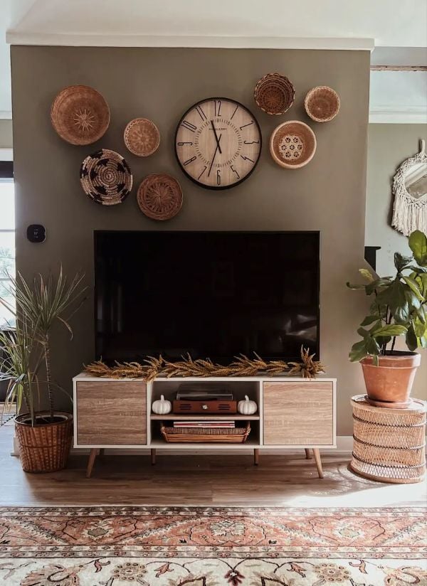 Living room TV wall with a large clock and woven baskets displayed above the television for cozy boho decor.