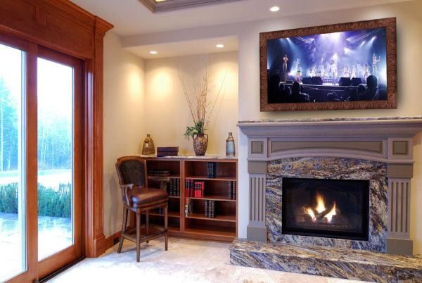 Framed TV mounted above a fireplace in a formal living room, designed to look like artwork when not in use.