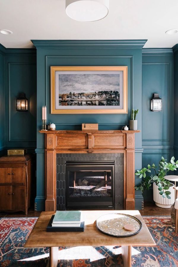 Teal fireplace wall with a framed TV displaying landscape art above a wood mantel.