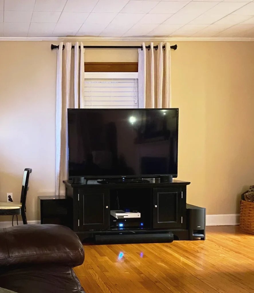 TV placed in front of a window with white curtains behind it, creating a soft curtain backdrop around the media console.