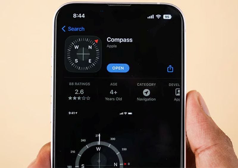 Hand holding an iPhone showing the Compass app page on the App Store with a navigation dial preview.