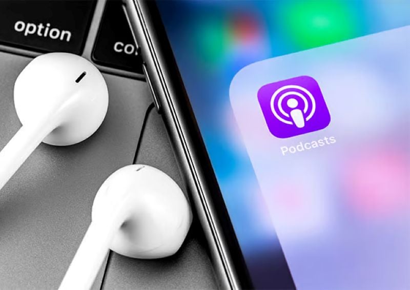 Close-up of iPhone screen displaying the Podcasts app icon next to a pair of white earbuds on a keyboard.