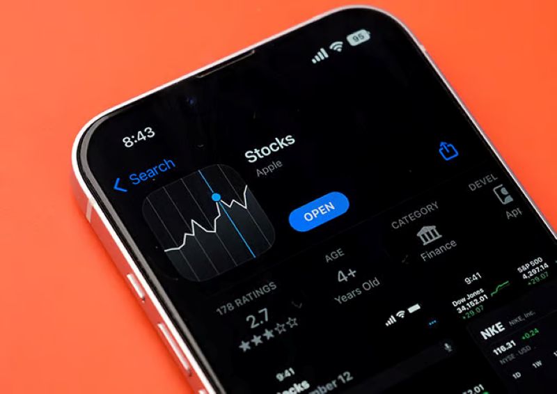 iPhone displaying the Stocks app page on the App Store with a graph icon against a bright orange background.