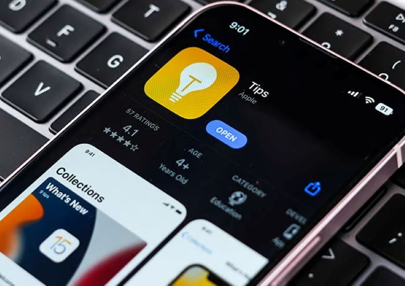 iPhone resting on a keyboard showing the Tips app page on the App Store with a yellow lightbulb icon.