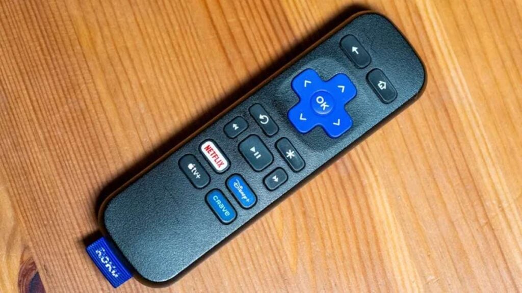 A Roku remote sitting on a wooden table, showing its buttons and slim design.