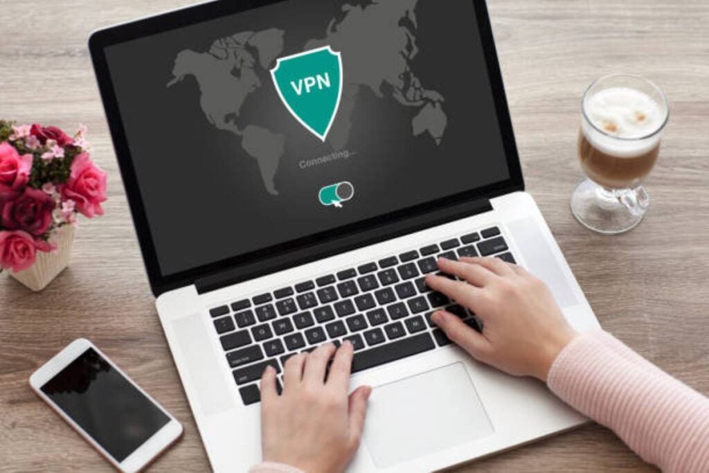Person using a laptop with VPN connection screen showing secure browsing on a desk with coffee and phone.