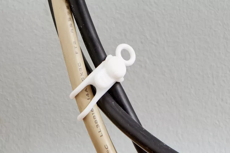 Close-up of black and beige cables secured with a white twist-style cord tie against a wall.
