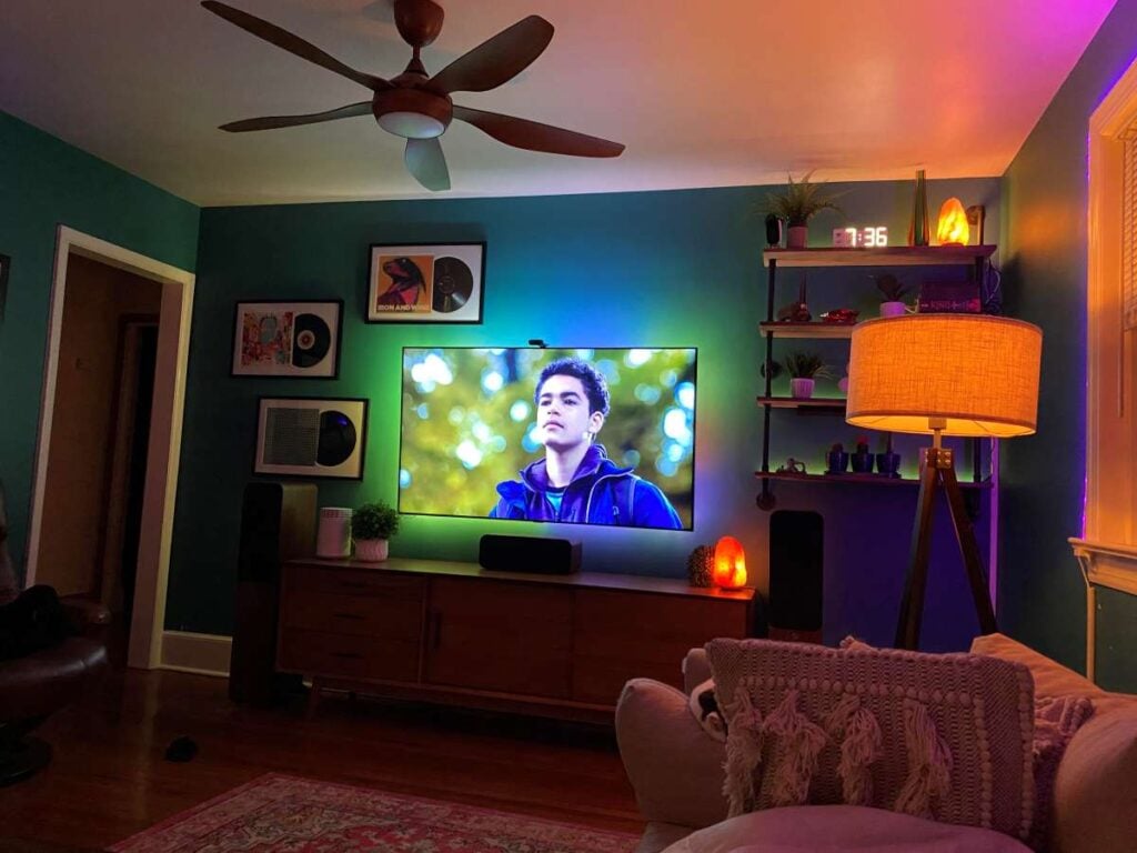 Cozy living room entertainment area with a wall-mounted TV, colorful backlighting, speakers, and low-cord devices on a media cabinet.