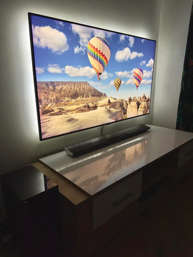 Wall-mounted TV with soft backlighting, a soundbar underneath, and hidden cords for a clean media setup.