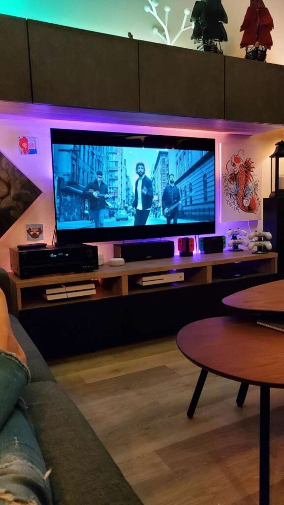 Home entertainment center with a TV, game consoles, speakers, and colorful LED lighting arranged with mostly concealed cables.