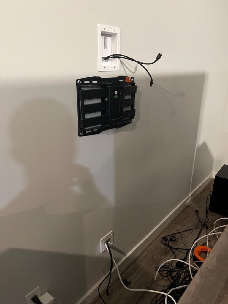 In-wall cable management kit installed behind a TV mount with upper and lower cable pass-through plates.