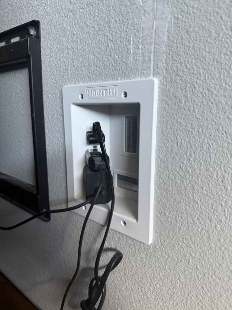 Close-up of a recessed wall plate with power outlets and cable pass-throughs for hiding TV cords.