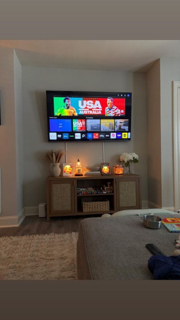 Wall-mounted TV above a wooden media console with a visible cord running down the wall.