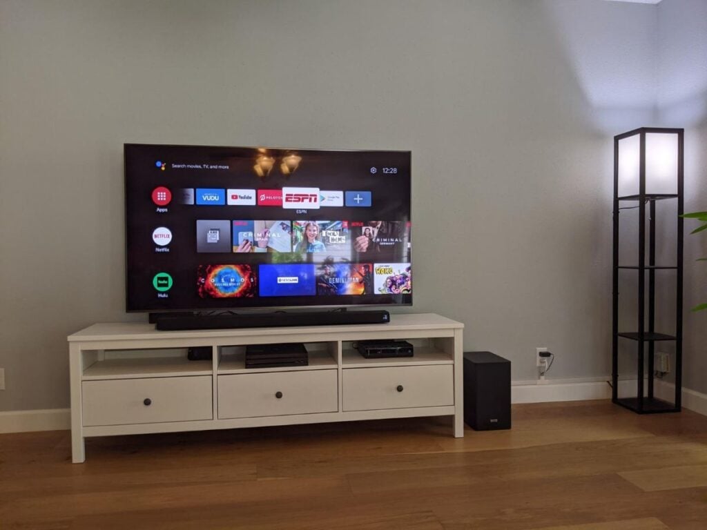 Flat-screen TV on a white media stand with cables and an outlet visible near the baseboard.