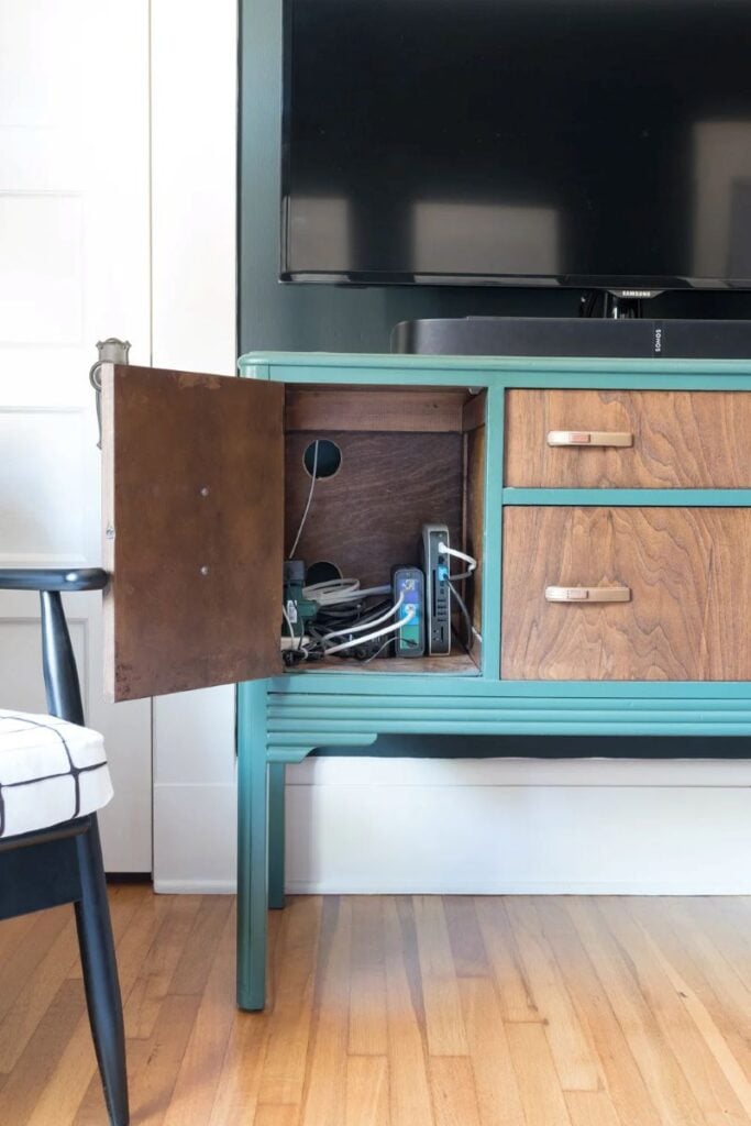 Media cabinet with an open side door showing hidden cords, router, and electronics tucked inside beneath a TV.